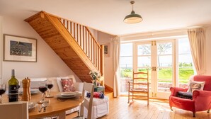 Un salon chaleureux avec un escalier en bois, une table à manger dressée avec des verres à vin et un fauteuil rouge.