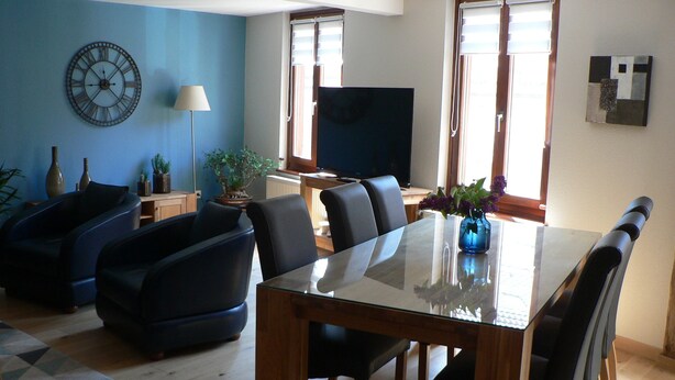 Una sala de estar moderna con comedor, que incluye un televisor de pantalla plana grande, asientos cómodos y un reloj decorativo en la pared.