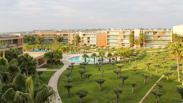 Ein Hotel mit Swimmingpool, umgeben von Palmen und gepflegten Rasenflächen.