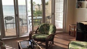 A living room with a view of the ocean, a ceiling fan, and a bookshelf. - Charming 2 bedroom 2 shower room self catering  apt on a gorgeous quiet beach (Fitts Village)