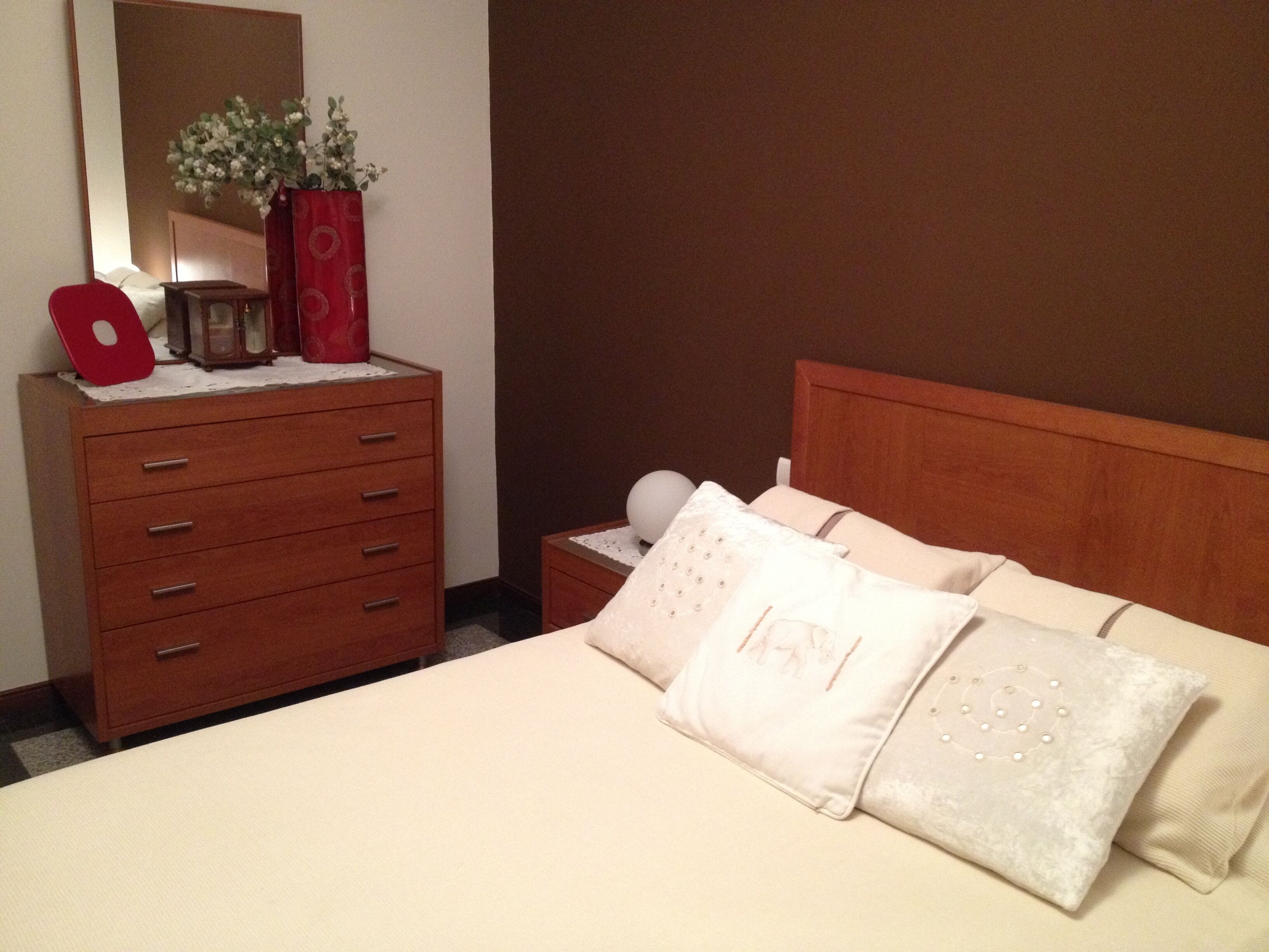 Ein ordentlich eingerichtetes Schlafzimmer mit einem Holzkapiton, einem Nachttisch mit Lampe und einem Bett mit vielen Kissen.