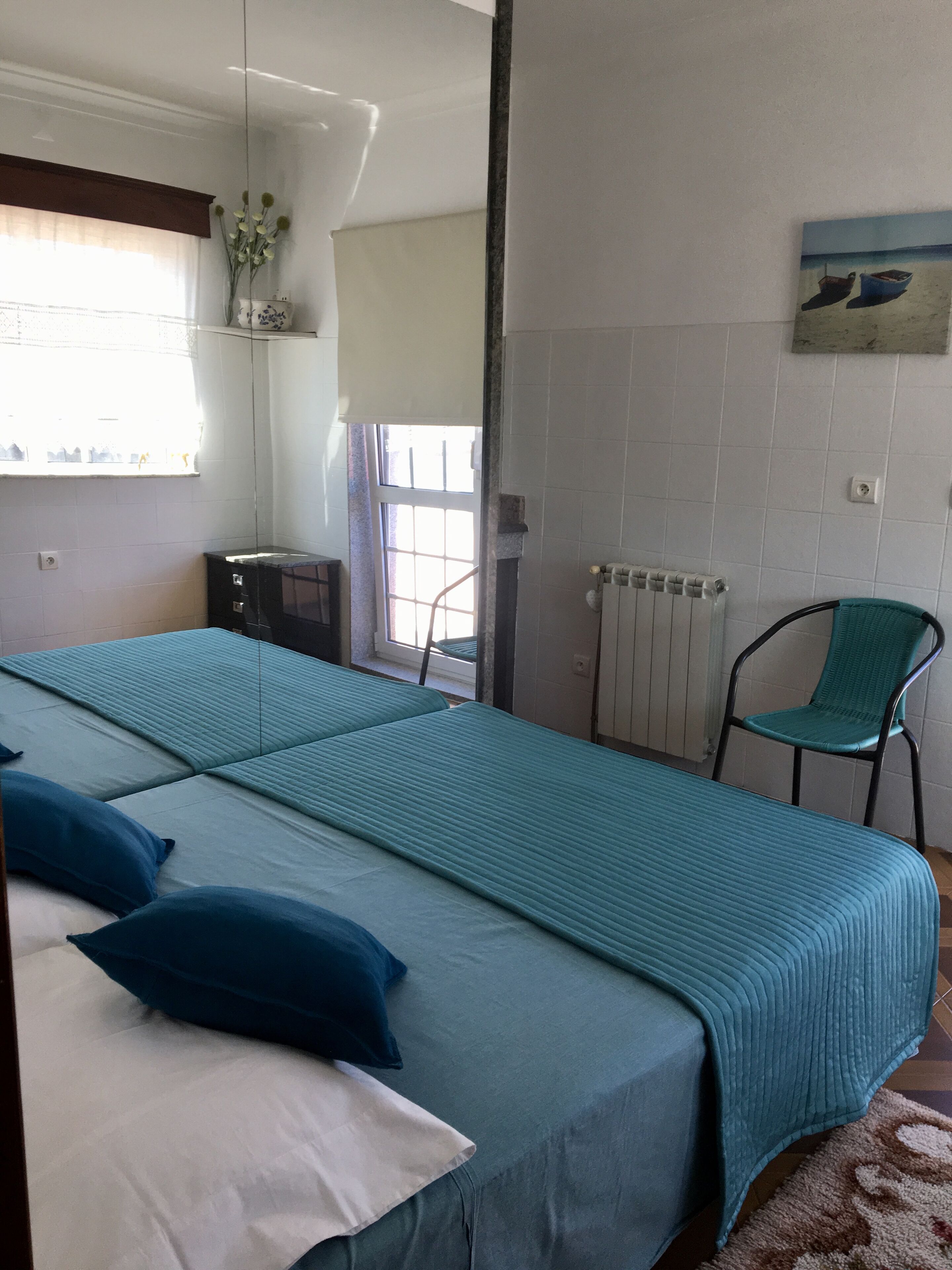 A room with a bed, a chair, a radiator, and a window with curtains.
