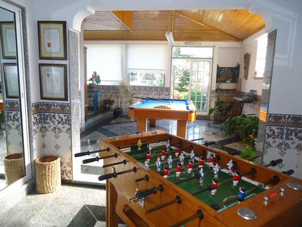 A room with a foosball table, a pool table, and a billiards table.