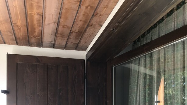 Et værelse med mørk trædør, stort vindue med gardiner og skråt loft.