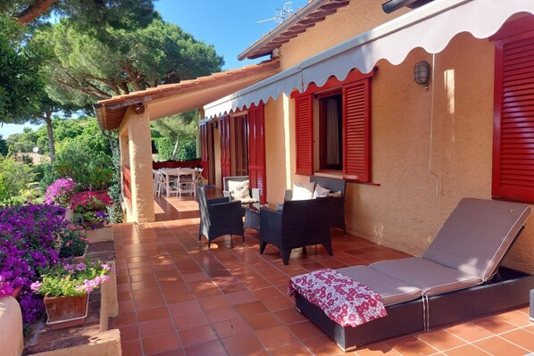 A covered patio with wicker furniture and a lounge chair, surrounded by potted plants and a tiled floor. - Villa Giolù: La Terrazza Apartment, near the beach ! (Portoferraio)