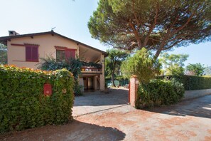 A house with a covered porch, a brick wall, and a large tree in front. - Villa Giolù: La Terrazza Apartment, near the beach ! (Portoferraio)
