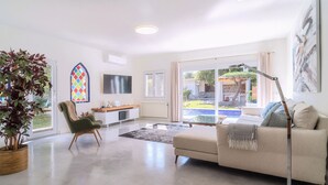 Una sala de estar moderna con un sofá, un sillón, un televisor, una planta y un ventanal con vistas al exterior.