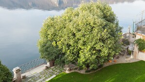 A well-maintained lawn with a stone pathway leading to a building, overlooking a calm lake with a town in the background. - Lakefront apartment with garden in the center of Orta San Giulio (Orta San Giulio)