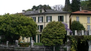 A waterfront property with a large building featuring a balcony, a garden, and a bridge over water. - Lakefront apartment with garden in the center of Orta San Giulio (Orta San Giulio)