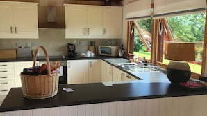 A kitchen with white cabinets, a black countertop, a wicker basket, a microwave, and a window with a view of greenery. - Comfortable Cottage With Spectacular Sea And Mountain Views (Duisdale)