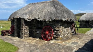 A traditional stone house with a thatched roof and red wooden wheels. - Comfortable Cottage With Spectacular Sea And Mountain Views (Duisdale)