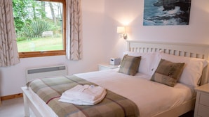 A bedroom with a bed, a bedside table, a nightstand, a window with curtains, a radiator, and a painting on the wall. - Comfortable Cottage With Spectacular Sea And Mountain Views (Duisdale)