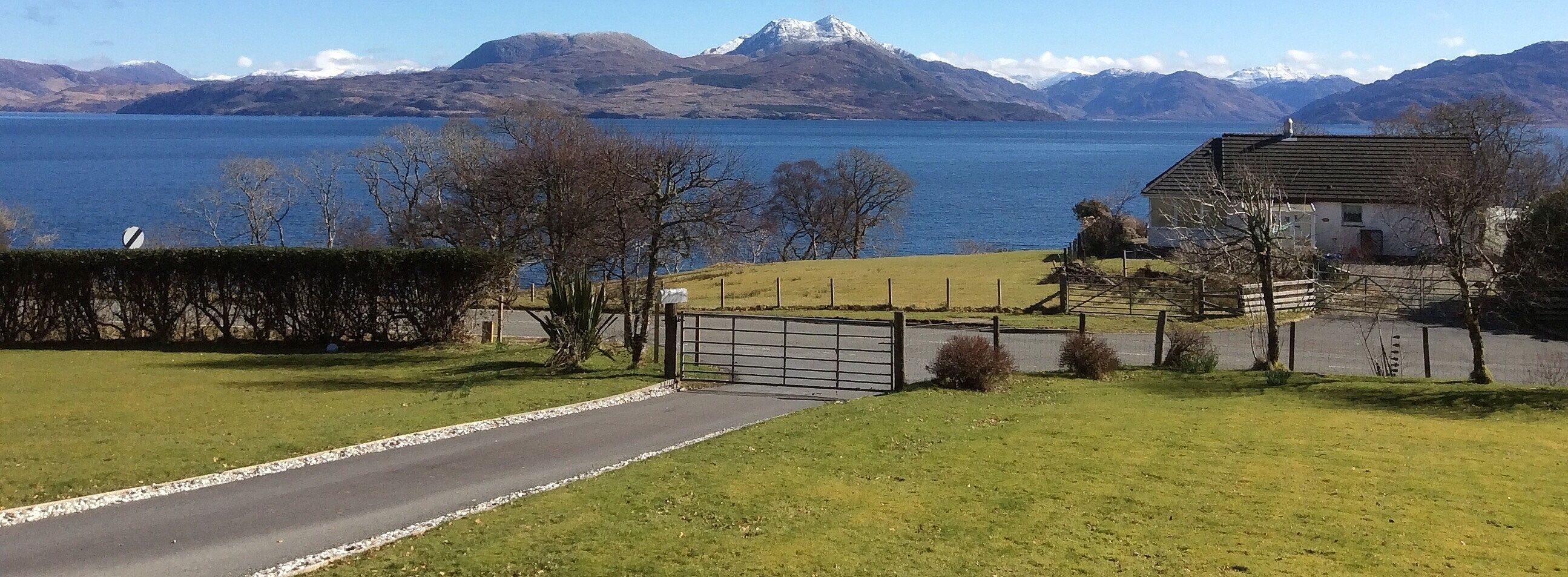 A rural road leading to a house with a view of a lake and mountains.