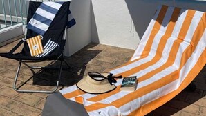 Eine Dachterrasse mit Liegestuhl in Streifenoptik, einem Klappstuhl mit gestreifter Sitzauflage und einem blauen Sonnenschirm.