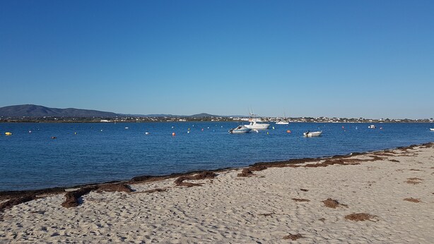 Ein Strand mit Booten auf dem Wasser und einer entfernten Bergkette.
