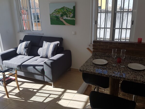 A living room with a grey sofa, a glass coffee table, and a painting of a landscape. - Wonderful house Built To Excellent Standards in the heart of Olhao. (Olhão)