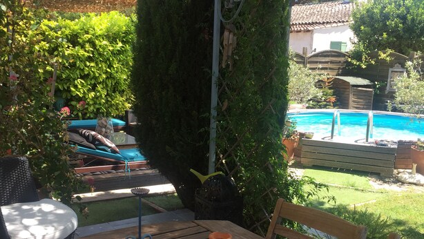A wooden table with a terracotta pot, surrounded by greenery and a pool in the background. - Charming villa with pool near downtown in quiet area. (L'isle-Sur-La-Sorgue)