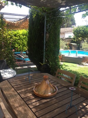 Ein Holztisch mit einem Terrakottatopf, umgeben von Grünpflanzen und einem Pool im Hintergrund.