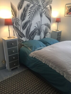 Ein Schlafzimmer mit einem Bett, zwei Nachttischen, einer Wandmalerei und einem gemusterten Teppich.