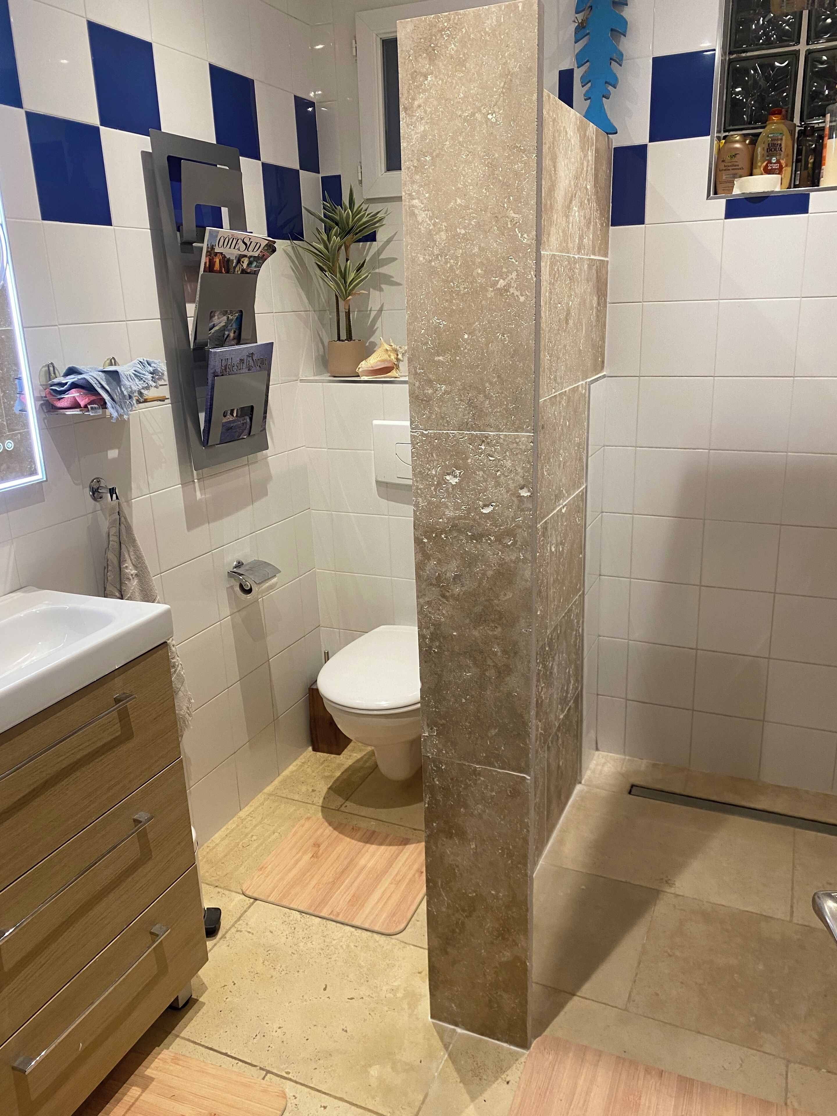 A bathroom with a white toilet, a sink with a towel, a mirror, and a shelf with toiletries.