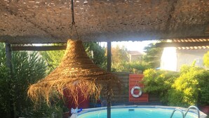A covered outdoor seating area with wicker furniture, a pool, and a thatched roof. - Charming villa with pool near downtown in quiet area. (L'isle-Sur-La-Sorgue)