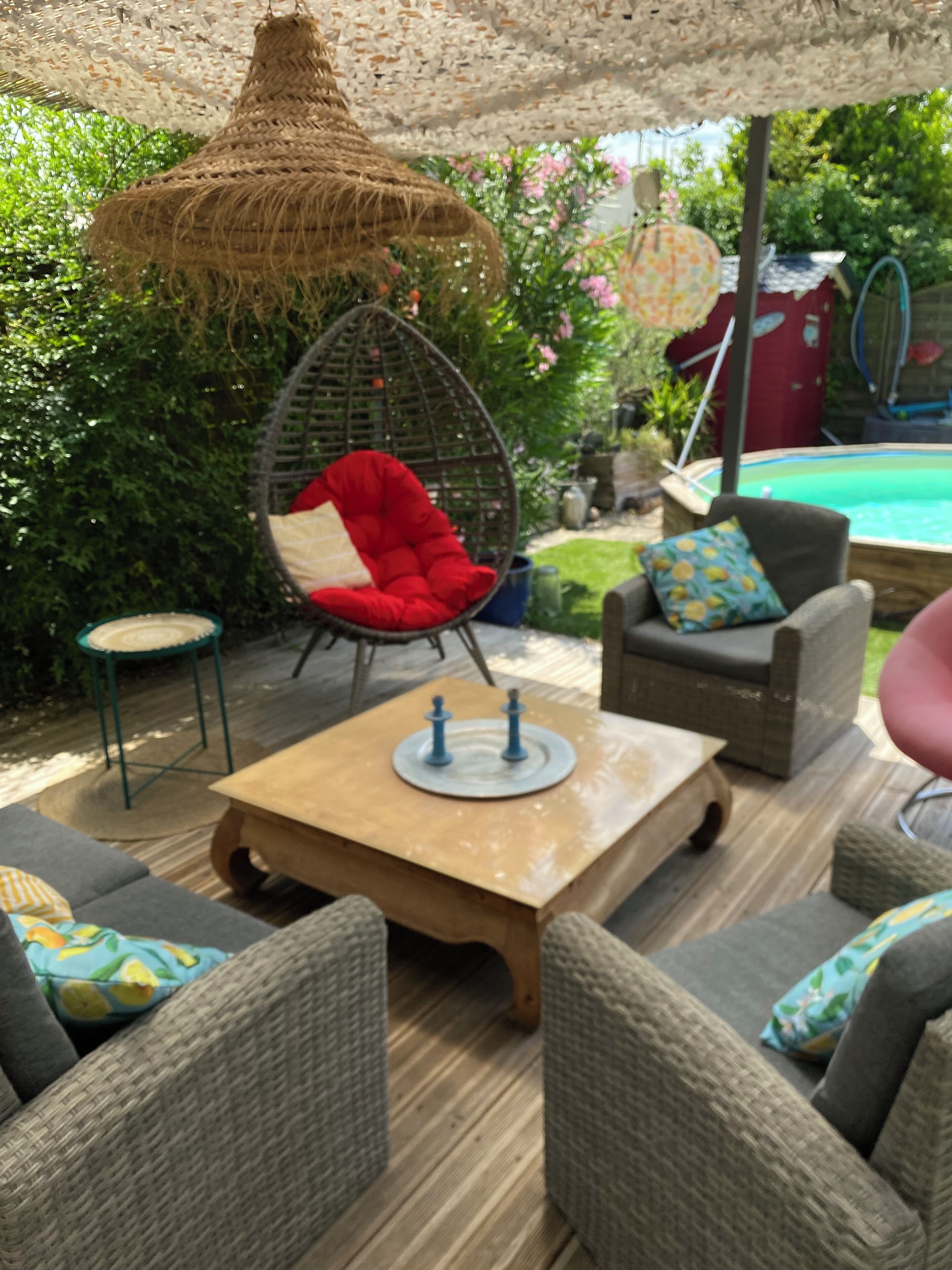 An outdoor seating area with wicker furniture, a hanging chair, and a table with chess pieces.