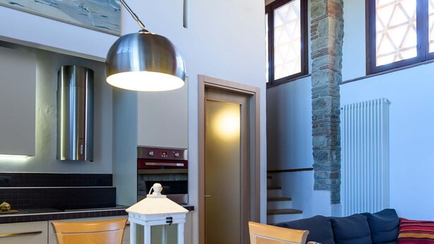 A modern kitchen with stainless steel appliances, a dining area with a table set for two, and a cozy living area with a dark sofa.