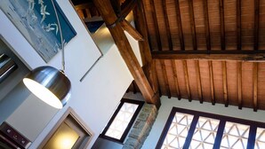 A room with a sloped wooden ceiling, a stone fireplace, and a large window with a grid pattern.