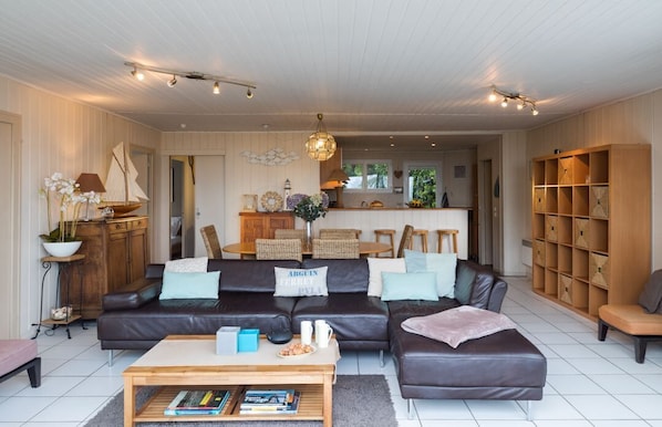 A modern living room with a dark leather sofa, a wooden coffee table, and a bookshelf. - stylish villa with beautiful sea view and heated pool (May to Sept) (Lège-Cap-Ferret)
