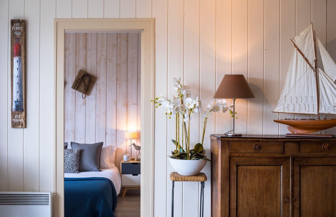 A room with a bed, a nightstand, a lamp, a cabinet, and a small table with a plant.