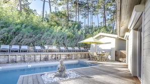 Une terrasse en bois avec une piscine, une statue et des chaises longues.