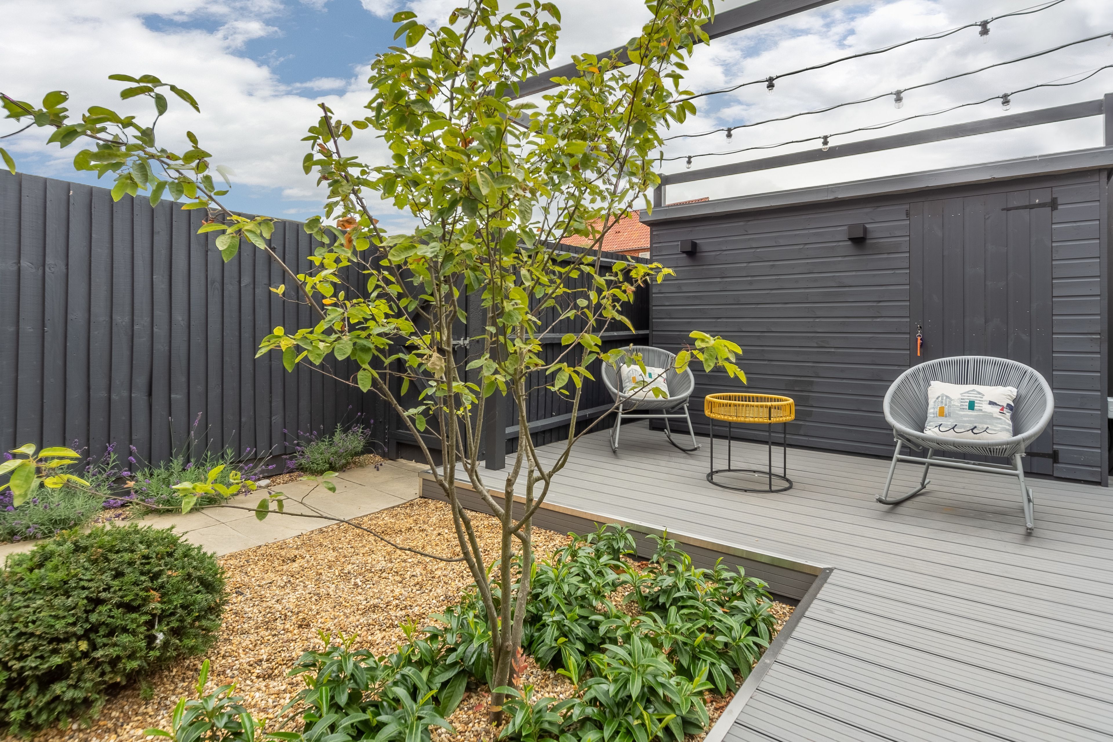 Une terrasse avec un petit arbre, une chaise et un panier jaune.