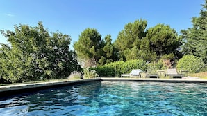 A clear swimming pool surrounded by lush greenery and trees.