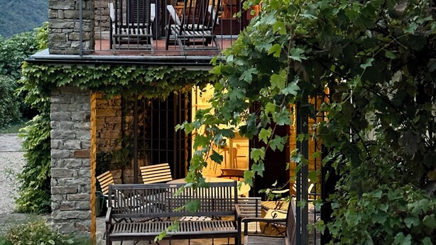 A stone house with a balcony, outdoor seating, and a view of the mountains.