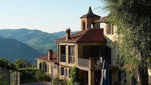 A stone building with a red-tiled roof, a balcony, and a view of the surrounding hills.