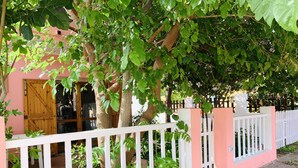 Ein pinkfarbenes Gebäude mit weißem Zaun, Bäumen und einem Holztor.