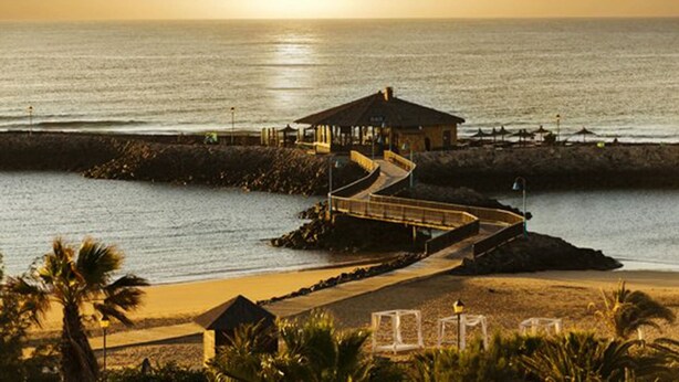 A coastal resort with a beach, a pier, and a small building with a thatched roof. - Luxury 3Bed Villa, Large Heated Pool, Wifi, Sun Terrace, Sea & Golf Course Views (Caleta De Fuste)