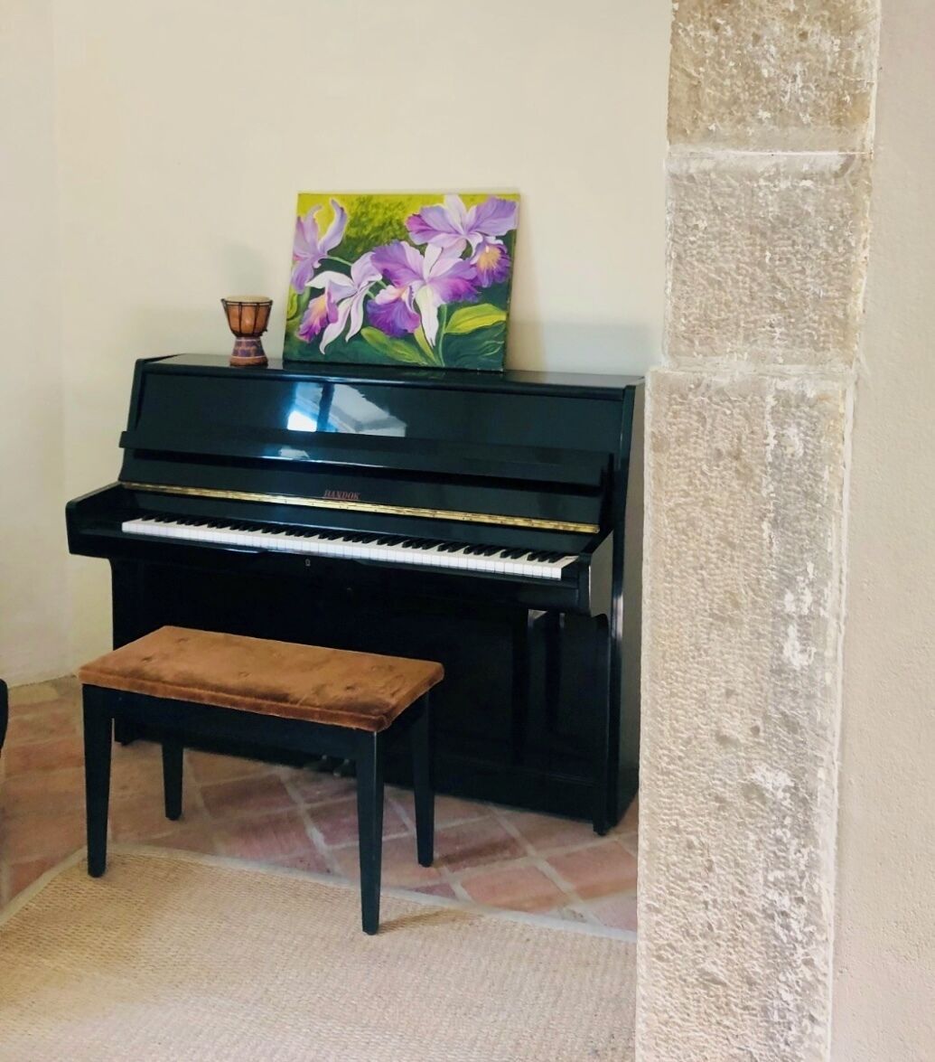 A piano with a bench in front of it, a painting above the piano, and a textured wall to the right.