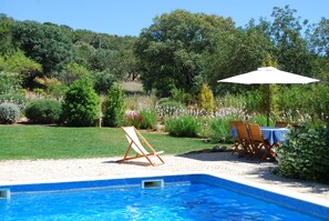 A swimming pool with a tiled edge, surrounded by a grassy area and trees. - Beautifully renovated typical Algarve villa (Bordeira)