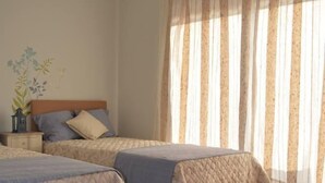 A bedroom with two beds, a wooden floor, a nightstand with a lamp, and a window with curtains. - “Musical View” – Fabulous view of the “Casa da Música” and surrounding area (Porto)