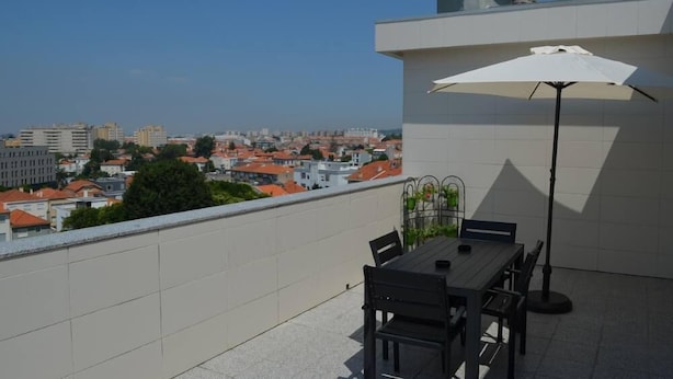 A rooftop terrace with a table and chairs, a white umbrella, and a city view. - “Musical View” – Fabulous view of the “Casa da Música” and surrounding area (Porto)