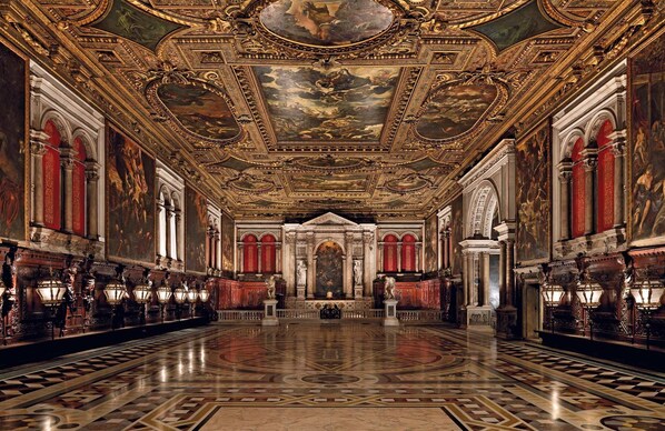 A grand hall with ornate ceiling frescoes, a central altar, and classical columns.
