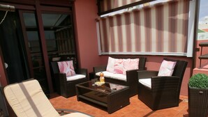 A patio with wicker furniture, a glass table, and a potted plant.