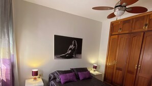 A bedroom with a bed, a ceiling fan, a wardrobe, and a wall-mounted picture.
