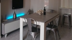 A modern dining area with a large table, four chairs, a TV mounted on the wall, and decorative lighting.