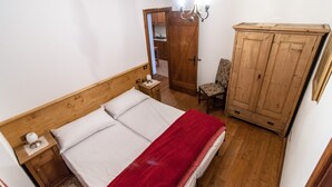 A bedroom with a wooden bed, a nightstand, a chair, a wardrobe, and a chandelier. - Adjacent to the pedestrian zone - 025016-LOC-01432 (Cortina d'Ampezzo)