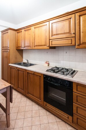 Une cuisine avec des meubles en bois, un évier en acier inoxydable, une cuisinière à gaz et un four noir.