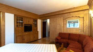 A room with wooden walls, a sofa, a TV, and a bed with a patterned bedspread. - Adjacent to the pedestrian zone - 025016-LOC-01432 (Cortina d'Ampezzo)