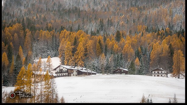 A snow-covered landscape with a cluster of buildings surrounded by autumn-colored trees and a forested mountain backdrop. - Adjacent to the pedestrian zone - 025016-LOC-01432 (Cortina d'Ampezzo)