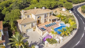 Ein zweistöckiges Haus mit Swimmingpool, umgeben von Grünflächen und einer gewundenen Zufahrt.